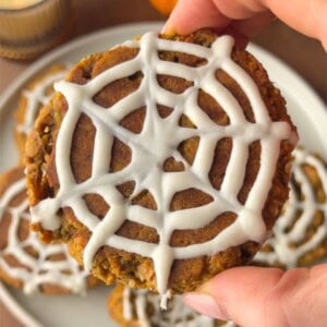 Soft pumpkin protein cookie topped with a white chocolate spiderweb design for an easy Halloween treat.