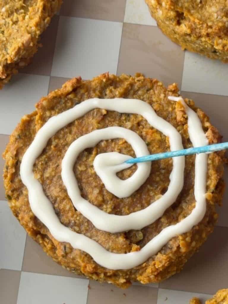 Pumpkin protein cookie being decorated with a white chocolate spiderweb using a toothpick.