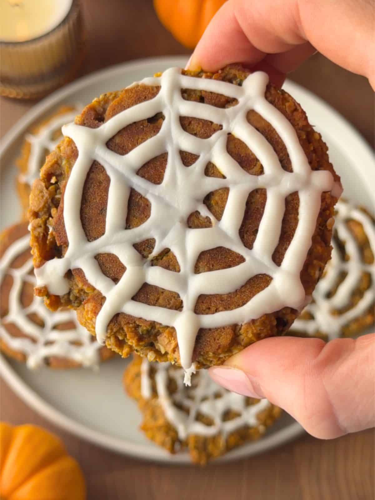 Soft pumpkin protein cookie topped with a white chocolate spiderweb design for an easy Halloween treat.